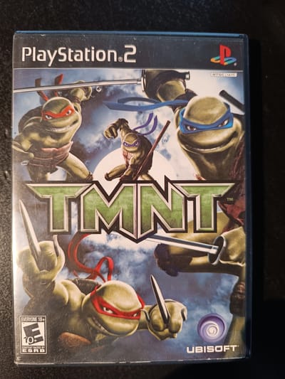 The media file is a cover for the video game "TMNT" for PlayStation 2. The cover art features the four Teenage Mutant Ninja Turtles in a dynamic, action-oriented pose. They are depicted as green, anthropomorphic turtles wearing masks and wielding their signature weapons: Leonardo with twin katanas, Michelangelo with nunchucks (partially visible), Donatello with a bo staff (partially visible), and Raphael with sais. The background is a cloudy, atmospheric sky, suggesting a battle is underway.

The Turtles are rendered in a realistic, slightly gritty art style. Their expressions convey intensity and readiness for combat. The title "TMNT" is prominently displayed in large, stylized green letters with a metallic border.

Visible text includes "PlayStation 2" at the top, along with the PlayStation logo. The "NTSC U/C" designation indicates the region compatibility. An ESRB rating of "EVERYONE 10+" is visible in the bottom left corner, with the "E" rating symbol. The Ubisoft logo is present at the bottom right.

The overall impression is one of high-energy action and adventure, characteristic of the Teenage Mutant Ninja Turtles franchise. The image is a close-up of the game's cover, with no discernible landscape or environmental details beyond the sky. No specific time of day or weather conditions are evident. The emotions conveyed are primarily determination and aggression.