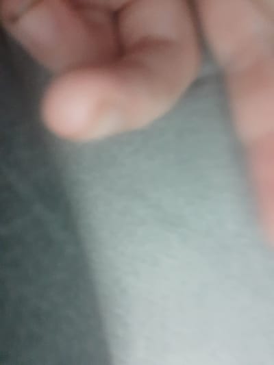 The image is a blurry, close-up shot of a person's hand. The background is out of focus and appears to be a textured surface in shades of gray and light blue. There are no identifiable landmarks or context that would allow for location determination within Liubakhy, Ukraine, or any other specific location. The image is too underexposed and lacking in detail to provide a forensic description of a scene.