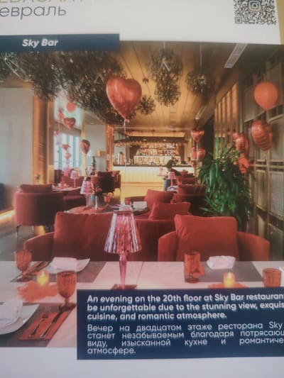 The image shows the interior of a restaurant called Sky Bar, decorated with red heart-shaped balloons. The restaurant features plush red seating and tables set with glassware and cutlery. In the background, a bar is visible, stocked with bottles. The text overlay indicates that this is "An evening on the 20th floor at Sky Bar restaurant," promising a "stunning view, exquisite cuisine, and romantic atmosphere." The Russian text below confirms this, describing an unforgettable evening at the Sky Bar restaurant on the twentieth floor, thanks to the breathtaking view, exquisite cuisine, and romantic atmosphere. The location is identified as Bahshitpa, Uzbekistan. There are no visible people in the foreground or mid-ground.