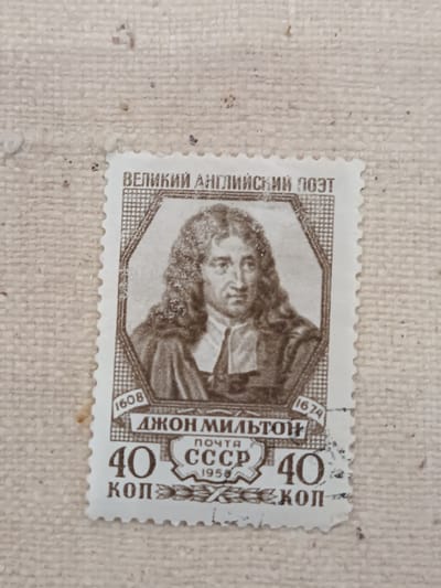 A postage stamp featuring a portrait of a man with long, curly hair and a ruffled collar. The man is depicted in sepia tones against a white background. The stamp has a serrated edge and contains Cyrillic text. The text at the top reads "ВЕЛИКИЙ АНГЛИЙСКИЙ ПОЭТ" which translates to "GREAT ENGLISH POET". Below the portrait, the name "ДЖОН МИЛЬТОН" is visible, translating to "JOHN MILTON". The stamp also includes dates "1608" and "1674", the word "ПОЧТА" (POST), "СССР" (USSR), and the denomination "40 КОП" (40 KOPEC). The stamp is affixed to a textured, light-colored surface, possibly fabric. There is no discernible connection to the city of Onaldy, Turkmenistan in the image.