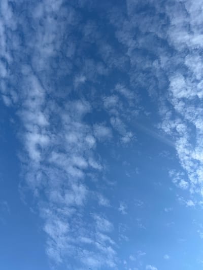 The image shows a wide-angle view of a bright blue sky filled with scattered, wispy white clouds. The clouds are thin and appear to be moving across the sky, creating a textured pattern against the clear blue. There are no visible structures, people, or other objects within the frame. The environment depicted is solely the sky. The location is Berestyn, Ukraine.