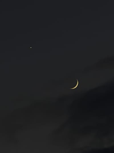 A crescent moon is visible in a dark, cloudy sky. To the left of the moon, a bright star is also visible. There are no people or objects in the image, nor are there any specific details about the location in Dongaron, Russia.