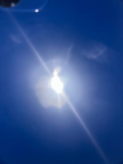 A bright light source, potentially the sun, dominates the center of the image against a clear, deep blue sky. Light flares radiate outwards from the central source. A dark, out-of-focus object is visible in the lower left corner. The location, Cheongju-si, South Korea, cannot be confirmed from visual data alone. No people, specific objects, actions, or interactions are discernible from this image.