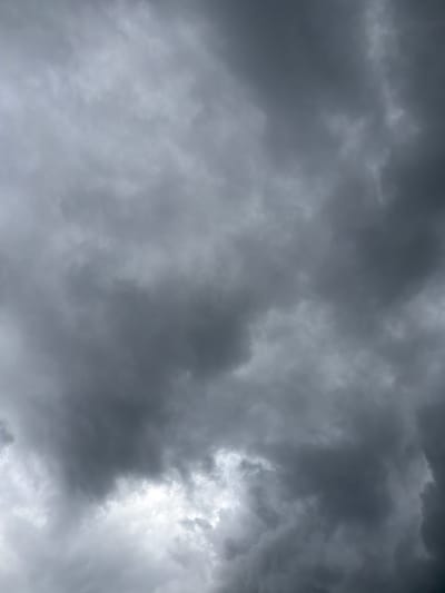 The image is a low-angle shot of a stormy sky filled with dark, heavy clouds. The clouds are thick and ominous, with varying shades of gray and black. There are some brighter areas where light is breaking through, suggesting a storm is either approaching or has just passed. The sky appears turbulent, with a sense of movement in the cloud formations. The scene depicts a natural environment, specifically the sky, devoid of any man-made structures or visible signs of human activity. The overall impression is one of dramatic weather conditions.