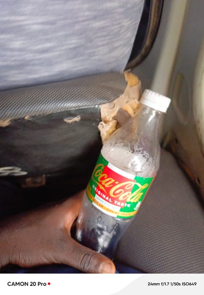 The image shows a close-up of a hand holding a bottle of Coca-Cola. The bottle is partially filled and has condensation on its exterior. The label on the bottle indicates "ORIGINAL TASTE" and "SUGAR · GREAT TASTE". The background appears to be a car interior, with worn upholstery visible. The image is taken with a CAMON 20 Pro, with camera settings of 24mm f/1.7, 1/50s, and ISO649.