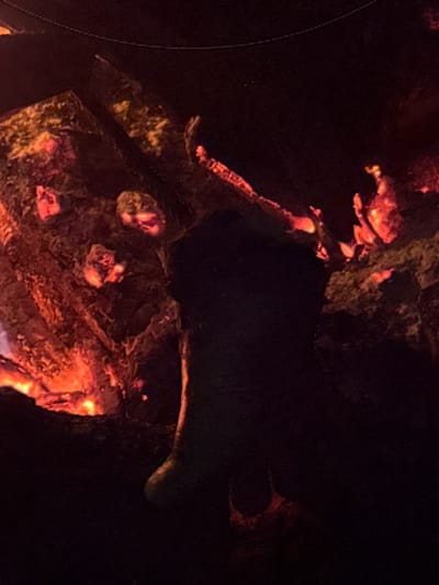 The image appears to be taken inside a dark cave in Carangsari, Indonesia. There are some illuminated portions of the cave with warm, reddish-orange light, which may indicate a light source like a torch or fire. The rock formations are visible where illuminated, but large portions of the cave are dark.