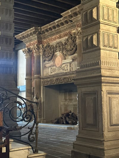 The image depicts an ornate, elevated architectural structure with heavily decorated elements. The structure features detailed carvings, including floral motifs, moldings, and panels with geometric patterns. There are columns and what appears to be coffered ceilings with recessed panels. The color scheme is primarily beige and brown. The style suggests a historical or religious building interior. A metal railing with decorative scrollwork is in the foreground. The location is most likely the Parish of the Body of Christ in the city of Tlalnepantla, Mexico. There are no people visible in the image. The environment is indoors, likely a church interior.