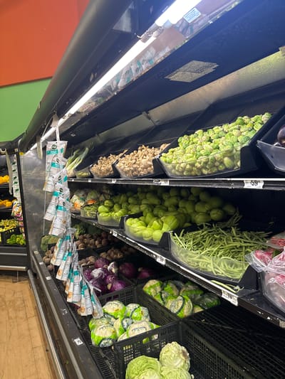 The image depicts a refrigerated produce section in a grocery store. Produce items include Brussels sprouts, chayote squash, green beans, purple cabbage, white cabbage, jicama, and other greens and root vegetables. "Ranch" brand salad dressing packets are also visible. Pricing labels are present on the shelves, showing prices like "$5.99" and "$1.19". Given the context of "Veracruz, Mexico", it can be assumed that the prices are in Mexican pesos. The image is rotated, suggesting it was taken with a mobile phone. The fluorescent lights and metal shelving are typical of grocery stores. No people are visible in the image.