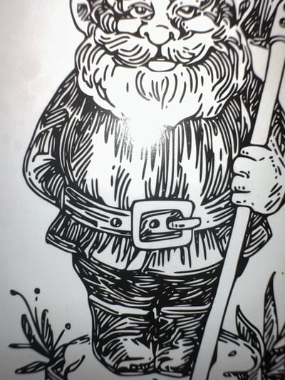 The image is a black and white illustration of a gnome, rendered in a linocut style. The gnome is depicted from the waist up, holding a long, thin object, possibly a staff or a tool, in its right hand. It has a prominent beard, a round nose, and its eyes are visible, suggesting a smiling or contented expression. The gnome wears a belted tunic with vertical stripes and appears to be wearing pants or breeches. The illustration is detailed, with fine lines used to create texture and shading. In the lower left corner of the image, there is a small, decorative sprig of leaves with two small dots, possibly representing berries or dew. The background is plain white, with some subtle photographic glare or artifacting visible. The image does not depict any identifiable landmarks or features of Letterkenny, Ireland, and therefore its location in the city cannot be determined from the visual information provided.