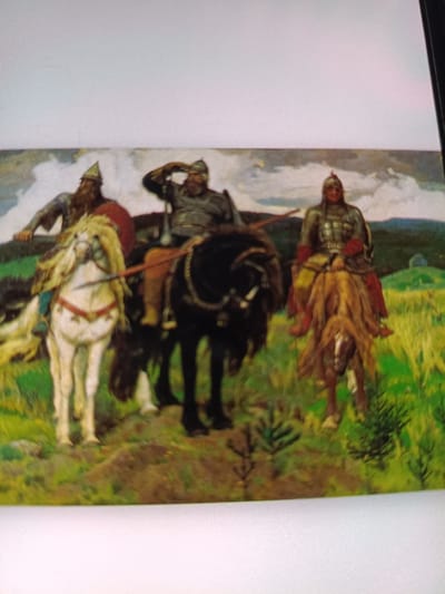 The image depicts a painting of three men on horseback in a grassy, hilly landscape under a cloudy sky. The man on the left rides a white horse, wearing a helmet and armor, with a red shield. He has a long beard. The central figure rides a black horse and wears a helmet and armor, with his right hand raised to his forehead as if shielding his eyes. The man on the right rides a light brown horse and is also armored, with red accents on his attire. The horses are depicted with flowing manes and tails. The overall scene suggests a historical or mythological theme, possibly a depiction of warriors or heroes. This artwork is displayed in the Zhovti Vody Museum of Local Lore in Ukraine.