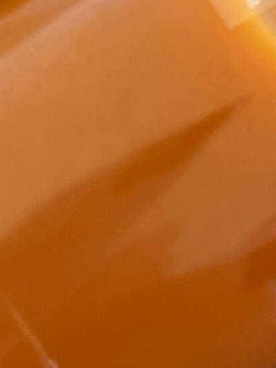 The image is a close-up, abstract shot of a smooth, glossy, orange-brown surface. The surface appears to be a solid material with subtle variations in color and texture, possibly indicating a reflective coating or a naturally occurring polished stone. There is a distinct shadow or gradient across the surface, suggesting a light source from the upper left. No people, animals, or specific objects are clearly identifiable. The image does not contain any elements that would allow for its location to be determined in Borowa, Poland, or any other specific geographical location.