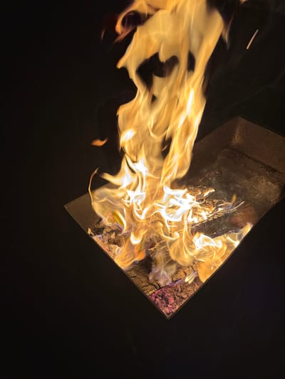 The image shows a fire burning inside a dark, rectangular container. Flames are exiting the container, extending towards the left side of the image. The container appears to hold wood and other fuel. The location of Mayak, Russia, is not directly discernible from the image. The scene depicts a fire within an enclosed space, with flames extending outward.