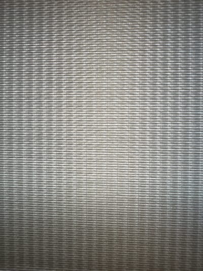 The image displays a close-up, full-frame view of a textured surface. The texture appears to be a repeating pattern of horizontal lines or ridges. The color of the surface is a neutral gray, with variations in shading that suggest lighting from above, creating highlights on the raised portions and shadows in the depressions. There are no people, animals, or identifiable objects visible in the image, nor is there any indication of a specific location within a city, including Izyayu, Russia. The scene is purely an abstract textural study.