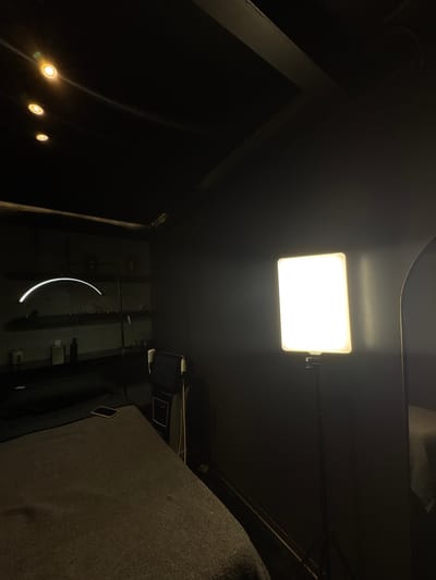 The image shows an interior space at night with artificial lighting. A rectangular LED panel light is mounted centrally on a dark ceiling. Further back, there is some lighting in the bottom left corner. On the right, a dark upholstered surface is visible, and toward the bottom a vertical wall runs upwards from the bottom edge to the middle. Further back a curved tube light illuminates the vertical wall. A monitor is fixed on the wall. I have no information to identify the specific location as Ciudad López Mateos, Mexico.
