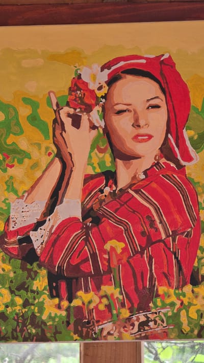 The image shows a painting in a frame. The painting depicts a woman lying on her side in a field of flowers. She is wearing a red headscarf and a red striped garment with lace trim on the sleeve. She is holding flowers in her hand. The background is a mix of green and yellow, suggesting foliage and flowers. The location cannot be determined solely from the image.