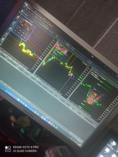 This is a medium-angle, eye-level shot of a computer monitor displaying a trading platform, likely for forex or cryptocurrency trading. The monitor is a Samsung brand, visible on the lower bezel. The screen displays multiple charts with price movements, indicators, and buy/sell signals. One prominent chart shows a "SMART TRENDLINE" indicator with a "BUY" signal and "ON" status. Another section of the screen indicates "Neuro Athena Current Signal: NO". The date "16.05.2020" and time "9:51" are visible in the bottom taskbar, suggesting the image was taken on this date and time. The surrounding environment is dimly lit, and the monitor is placed on a desk or table. The background texture appears to be a patterned wallpaper. There are no people visible in the image. The metadata on the bottom left corner indicates "REDMI NOTE 8 PRO AI QUAD CAMERA", suggesting the photo was taken with this mobile device. The location of Irbit, Russia is not discernible from the image itself.
