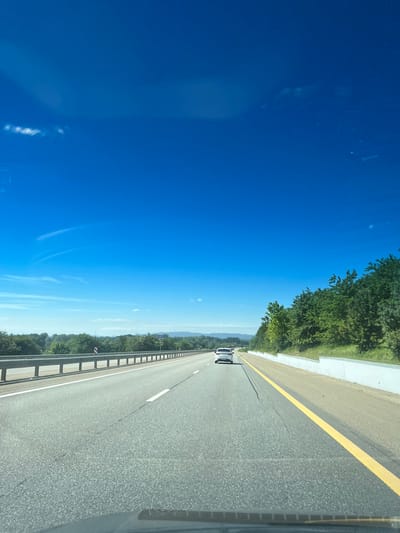 The image depicts a view from inside a vehicle on a highway. The highway is paved and has lane markings. Another vehicle is visible ahead. The surrounding environment includes trees and a clear blue sky. The location is Saratovskaya, Russia, as indicated by a road sign marked 1377.
