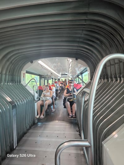 The image depicts the interior of a bus, as indicated by the rows of seats, windows, and overhead luggage racks. Several passengers are visible, mostly seated and some engaged with their mobile phones. The distinctive ribbed ceiling and metallic interior suggest a modern design. The presence of the text "Galaxy S26 Ultra" in the lower left corner of the image indicates it was taken with a Samsung phone. The text overlaid on the image, "Galaxy S26 Ultra", strongly suggests this image was taken on a Samsung Galaxy S26 Ultra phone. The specific location of Llucmajor, Spain, is not visually evident from the image itself. The bus appears to be in motion or stopped at a station, with passengers either commuting or on a journey. The overall atmosphere is ordinary and unremarkable, capturing a typical scene within public transportation.