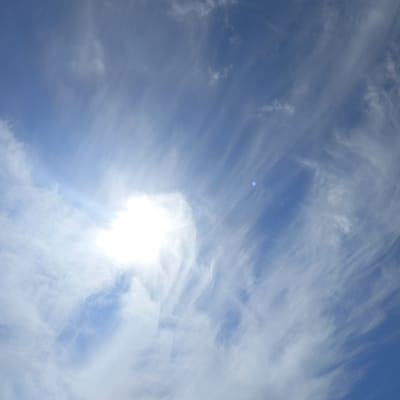 The image shows a bright, daytime sky with wispy white clouds streaking across a clear blue expanse. The sun is visible in the upper left quadrant, casting a bright glow that washes out some of the surrounding clouds. There are no discernible landmarks or features in the sky that would indicate a specific location within Ballybunnion, Ireland. The scene is solely focused on the sky and its atmospheric conditions.
