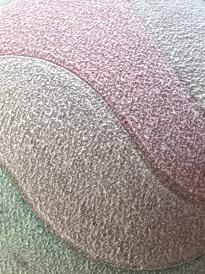 The image shows a close-up of a textured fabric with distinct color blocks. A light pink or dusty rose section curves over a grey section. Below the grey section, a light teal or mint green section is visible. The texture appears to be consistent across all colors, suggesting it is a single material or a very similar set of materials. The image is a cropped, abstract view and does not provide any contextual information about its location in Bad Hersfeld, Germany, or any identifiable subjects or objects.