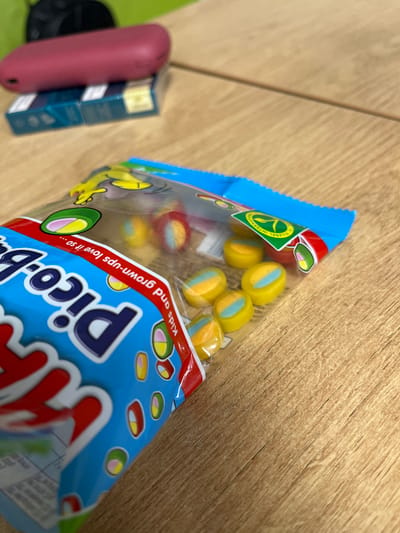 The image shows a bag of "Pico-B" jelly beans on a wooden surface. A red object, possibly a vape device, rests on a pack of cigarettes in the background. The scene appears to be indoors, on a table. The location of Gorni Dabnik, Bulgaria, is not discernible from the image.