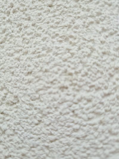 The image is a close-up, abstract shot of a textured, off-white surface, possibly stucco or a rough plaster. The texture is uneven with small bumps and indentations creating a mottled pattern. The lighting is diffuse, casting subtle shadows that emphasize the relief of the surface. There are no discernible objects, people, or environmental features present. The image does not provide any information about a specific location in Rzeszów, Poland.