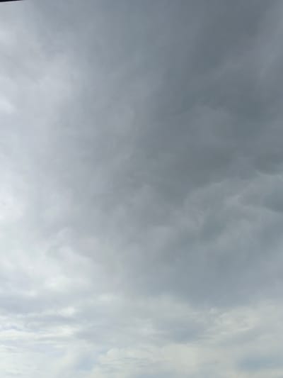 The image displays a vast expanse of overcast sky, with a gradient of gray and white clouds. The clouds are textured and varied in density, with some appearing more wispy and translucent while others are thicker and darker. There is no discernible land or city visible in the frame, only the sky. The lighting suggests it is daytime, but the heavy cloud cover creates a diffused and somewhat somber atmosphere. There are no people, objects, or any specific actions or interactions evident in this photograph. The context of "Tecnimont camp, Russia" is not visually represented in the image itself.