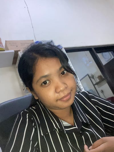 A person with dark hair is wearing a black and white striped shirt. The background includes a white wall, a window, and a box with the words "Wonderful Gift" on it. The location is Negara, Indonesia.