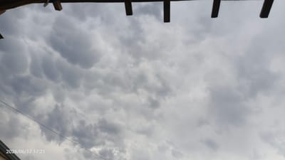 This media file captures a dramatic sky filled with mammatus clouds, a rare and striking meteorological phenomenon. The clouds appear as a series of rounded pouches hanging from the underside of a larger cloud. The overall color palette is dominated by shades of gray, indicating an overcast or stormy weather condition.

In the foreground, parts of a wooden structure are visible at the top of the frame, suggesting an outdoor setting like a patio, pergola, or covered walkway. A thin black wire, possibly a power line or telephone cable, stretches diagonally across the lower portion of the sky.

The timestamp "2026/06/17 17:21" is overlaid on the bottom left corner of the image, providing specific date and time information. The light suggests it is late afternoon. The overall mood is one of awe and perhaps a hint of foreboding due to the unusual cloud formation and the overcast sky. The location context is identified as Margilan City, Uzbekistan. No people are visible in the image.