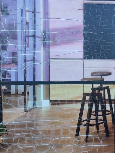 The image depicts an indoor scene with a modern aesthetic, featuring a dark-colored bar stool in the foreground. The stool has a wooden seat and a metal base with footrests. Behind the stool, a horizontal black bar stretches across the image, separating the foreground from the background. The background consists of a wall with wooden paneling in a light pink hue, and to its right, a dark textured surface, possibly a chalkboard or a dark panel. To the left of the pink paneling, a reflective surface shows a distorted view of shelves and vertical elements in shades of purple and white. The floor in the foreground is tiled with a stone-like pattern in shades of brown and beige, with visible grout lines. The entire image appears to be overlaid with a cracked or textured effect, creating a distressed visual. The scene is observed from a straight-on perspective. There are no people visible in the image. The image is identified as being located in Bielany Wrocławskie, Poland.