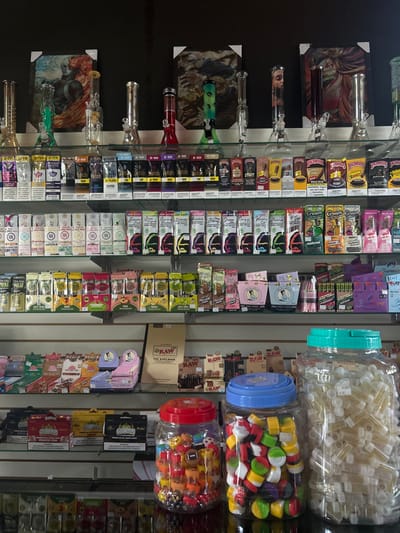 The image shows a retail store in Cobano District, Costa Rica, located at the coordinates 9.635 latitude and -85.158 longitude. The store is a cannabis dispensary, as evidenced by the various products on display, including cannabis cigarettes, pre-rolled joints, bongs, grinders, rolling papers, and other cannabis paraphernalia. The store shelves are organized and stocked with a wide variety of cannabis products, including different brands and types of pre-rolled joints, rolling papers, and other smoking accessories. There are also several large jars filled with small glass tubes, likely intended for use in consumption of cannabis. The store's interior is clean and well-lit, and there are various artistic prints on the walls, including depictions of marijuana leaves, cannabis plants, and other cannabis-related imagery. The store is likely designed to appeal to cannabis consumers, and the products on display suggest that the store is catering to a wide range of cannabis users.