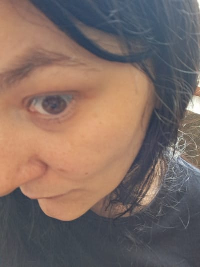 The image is a close-up, low-angle shot of a person's face, focusing on their eye and nose. The subject has dark hair that is partially obscuring their face. The lighting suggests an indoor environment, likely a home, given the soft, diffused light and the presence of what appears to be textured upholstery in the background. The person is wearing a dark-colored shirt. The overall impression is of a casual, personal photograph, with no indication of an outdoor setting or any specific landmarks in Marchevo, Bulgaria.