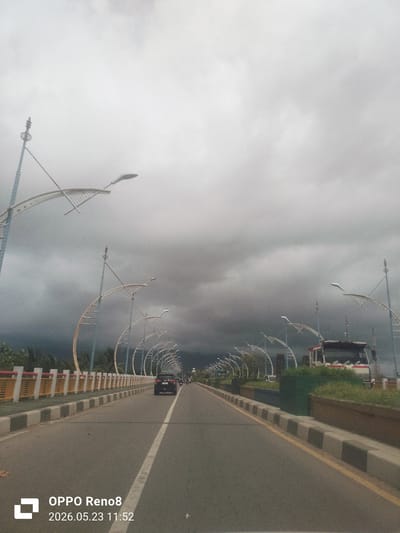 The image shows a road bridge in Lambaro, Indonesia, under a cloudy sky. The bridge has a center white line and bordered sides. On the bridge, there is a car, a truck and other vehicle are visible. Ornamental light fixtures are mounted along the bridge sides. The timestamp "2026.05.23 11:52" is at the bottom left.