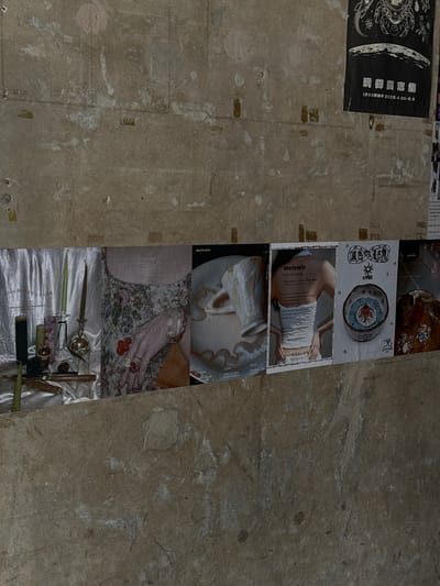The image shows a series of flyers or posters adhered to a rough, uneven surface, possibly a wall or floor. The posters appear to be advertising an event, "Meiewie POP UP STORE," which is taking place from April 18th to July 15th, 2025. The posters contain images of various objects, including jewelry, decorative pottery, and vintage items. In the upper left corner, a poster reads "玩物丧志集 1933老編 2025.4.30-5.5" with the date of "2025.4.30-5.5". It appears to be in Hongkou District, China.