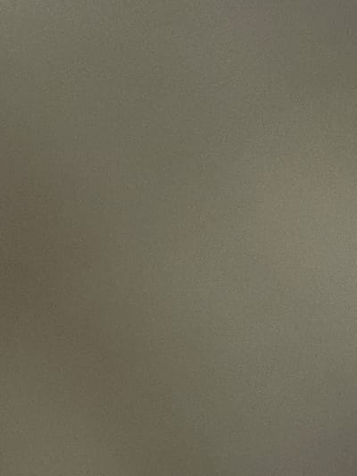 The image shows a close-up of a textured, dull, neutral-colored surface. The texture appears to be granular or slightly rough, with subtle variations in shade across the frame. There are no discernible objects, people, actions, or interactions visible in the image. The background is uniform in color and texture. No location in Kassa, Nigeria can be identified from this image.