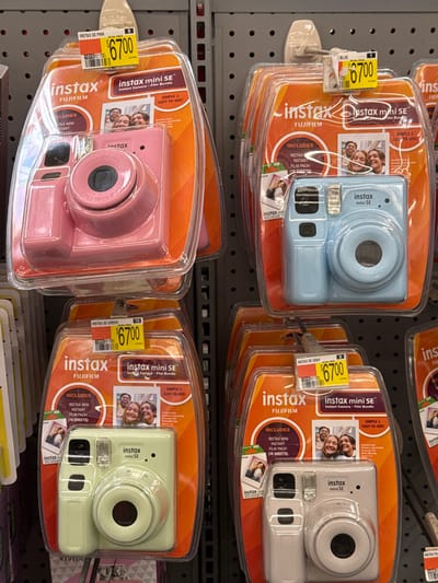 This image displays a retail store shelf showcasing multiple Fujifilm Instax Mini SE instant cameras, likely in Worcester, United States. The cameras are neatly arranged on metal display hooks, presented in clear plastic packaging. Four distinct colors are visible: blue, gray (appearing white), pink, and a light green.

Each package is branded with "instax" and "FUJIFILM" logos and identifies the product as an "instax mini SE Instant Camera + Film Bundle." Prominently featured text on the packaging highlights "SIMPLE & EASY-TO-USE!" and specifies that each bundle "INCLUDES INSTAX MINI INSTANT FILM PACK (10 SHEETS)." Images of smiling individuals and couples on the packaging illustrate the type of happy moments these instant cameras are designed to capture.

Price tags are attached to each product, clearly showing "$67.00" and specifying the color of the camera, such as "INSTAX SE BLUE," "INSTAX SE GRAY," "INSTAX SE PINK," and "INSTAX SE GREEN." The scene depicts a typical retail environment, with the products presented for sale. No people are physically present in the frame, but the implied activity is shopping for instant cameras. The lighting suggests an indoor setting.