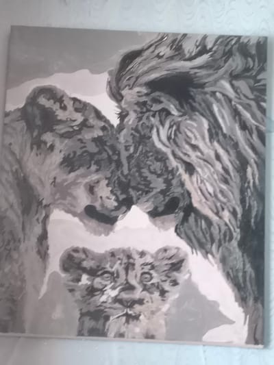 This media file is a photograph of a monochromatic painting featuring a family of lions. The painting depicts a male lion with a prominent mane on the right, leaning in towards a lioness on the left. Their heads are close together, suggesting an intimate interaction. In the foreground, a lion cub is visible, looking directly at the viewer with wide eyes. The overall tone of the painting is somber and familial, with the lions appearing to be in a moment of quiet connection. The background is abstract and lacks specific detail, allowing the focus to remain on the lion family. The style of the painting is realistic with bold brushstrokes, creating a textured effect. No text is visible in the image, and there are no specific cues to indicate the time of day, weather, or a precise location beyond what is implied by the subjects themselves.