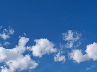 The image shows a blue sky with white clouds and a contrail from an airplane. The clouds are mostly concentrated in the lower half of the image. The contrail is in the upper right quadrant. The location is not discernible as Zverino, Bulgaria.
