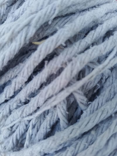 This is a close-up, macro photograph of a light blue mop head. The image focuses on the texture and weave of the mop strands, which are thick and appear to be made of synthetic fibers. The strands are arranged diagonally across the frame, creating a pattern of lines and shadows. There is a slight blur to the image, suggesting a shallow depth of field. No people, actions, or interactions are visible. The environment is not discernible beyond the texture of the mop. There is no information in the image that would allow for the identification of a location in Nicorești, Romania, or any other specific geographic location.