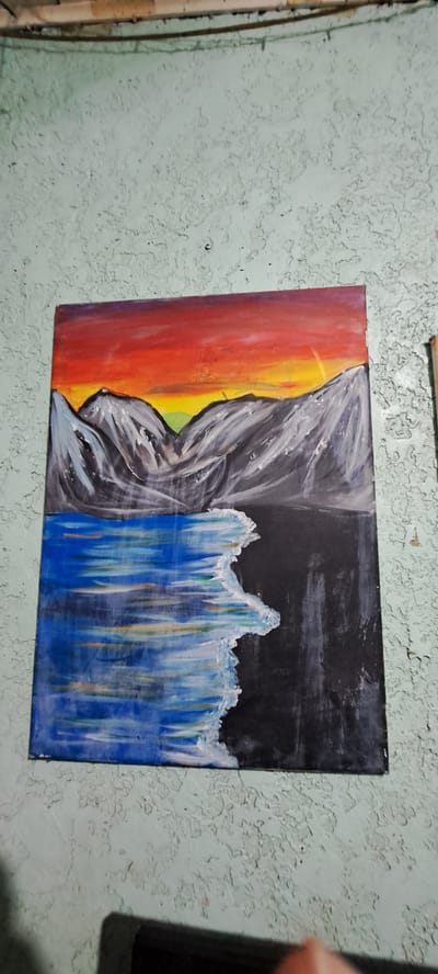 The image shows a painting of a sunset over mountains and a body of water, mounted on a textured, light green wall. The painting features a vibrant sunset with orange, red, yellow, and purple hues. In front of the sunset are stylized grey mountains. The lower half of the painting depicts a body of water with blue and white streaks, suggesting waves or ripples, and a dark, reflective surface on the right side, possibly indicating depth or a shadowed area. The wall has a rough, peeling texture, characteristic of older paint or plaster. There are cables or wires running horizontally along the top edge of the wall, above the painting. The painting is the primary subject, positioned centrally on the wall. The overall scene suggests an indoor setting, possibly a home or studio, where the artwork is displayed. The location of Mandaluyong City, Philippines is not ascertainable from the visual information provided in the image.