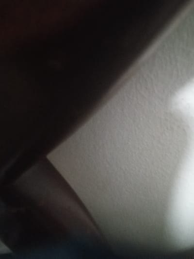 The image is a close-up of a wall, possibly inside a building. The wall is a light grey color and appears to be textured, with visible fibers. A large, dark shadow covers most of the image, suggesting a nearby object or an overhead light source. The coordinates provided are for a location in Santo Domingo, Dominican Republic. However, the image itself does not contain any identifying features that would allow for a specific location within the city.