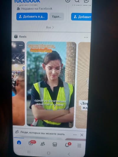 The image shows a smartphone screen displaying a Facebook interface, specifically the Reels section. The screen is oriented vertically. In the foreground, at the bottom of the screen, are navigation icons for the Facebook app, including a home icon, a notification icon with "99+" and "4" counts, a group icon, and a shop icon. Above this, there is a section labeled "Люди, которых вы можете знать" (People you may know). The main content area displays a Reel video featuring a woman in a yellow safety vest. Text overlays on the video read "Озвучка | Тайна сестры | Королева водительница" and "watch for free". Another Reel is partially visible to the left, showing the back of a man's head in what appears to be a store setting. A third Reel is partially visible to the right with text that is largely obscured. The overall context is a social media feed on a mobile device. There is no information within the image that indicates a location in the city of Korolevo, Ukraine.