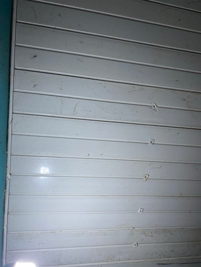 The image depicts a close-up view of a white, panelled ceiling. Fasteners, some missing or damaged, are visible along the seams between the panels. The panels show signs of wear and dirt. A light source is visible in the bottom right corner. The location is Sabo, Nigeria.