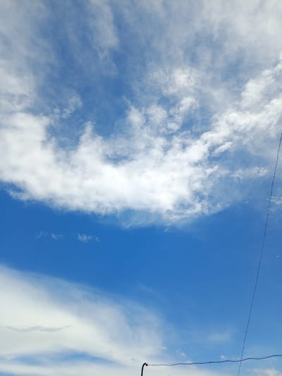The image captures a vibrant blue sky dotted with scattered white clouds. The clouds are thin and wispy in some areas, while others are more dense and fluffy, suggesting a partly cloudy day. The overall impression is one of a bright, sunny day, likely in the late morning or early afternoon given the clarity of the sky.
A thin, dark wire runs diagonally across the right side of the frame, a subtle indication of human infrastructure within the natural scene. Another segment of wire, also dark, is visible in the lower portion of the image, appearing to connect to an unseen structure. These elements suggest an outdoor setting, possibly overlooking a landscape or from a balcony or rooftop.
There is no visible text in the image. The scene evokes a sense of calm and openness, characteristic of a clear sky on a pleasant day. The location context of Otradnaya, Russia, is not directly evident from visual cues within the image itself, but it provides a geographical setting for this natural phenomenon.