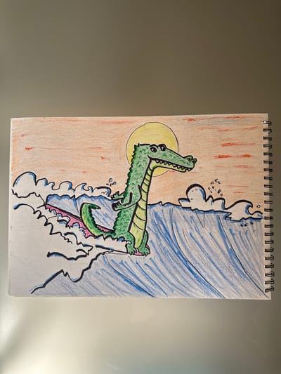 A hand-drawn, colored-pencil illustration on a spiral-bound notebook page depicts a cartoon alligator emerging from swirling blue water. The alligator, colored green with black outlines and yellow accents on its belly and inside its mouth, appears to be lunging forward. Its mouth is open, revealing rows of sharp teeth and a pink tongue. Small, scattered blue bubbles are shown near the alligator's head, suggesting movement in the water.

To the left of the alligator, a bright yellow circle represents the sun, set against a background of soft orange and red vertical strokes, possibly indicating a sunset or sunrise. The water on the right side of the page is depicted with varying shades of blue, with white highlights and dark blue outlines forming waves and spray. The bottom of the illustration features white, abstract shapes with black outlines, possibly representing foam or crashing waves. The illustration is framed by the white spiral binding of the notebook at the top of the page. No text is visible in the image. The overall scene suggests a dynamic and somewhat dramatic moment, possibly a playful or powerful emergence of the alligator from the water.