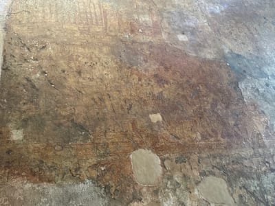 The image depicts a deteriorated fresco on a wall, likely located within an ancient structure. Faint outlines of figures, possibly religious icons or scenes from a narrative, are visible in the upper left quadrant. The wall's surface is heavily weathered, exhibiting cracks, flaking paint, and areas of discoloration. Patches of the fresco appear to have been filled in with modern plaster, suggesting preservation efforts. The setting is consistent with historical sites in Polonnaruwa, Sri Lanka, known for its ancient ruins and frescoes. There are no people or clear objects. The subjects are religious figures in the fresco. Actions might have occurred on the fresco. Interactions are religious. The environment consists of walls with the fresco.
