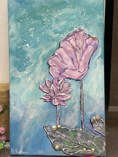 The image shows a close-up, eye-level view of an acrylic painting on canvas. The painting depicts two stylized purple lotus flowers, one large and one small, with textured petals. The background is a vibrant teal and blue with white splatters and some reddish-brown speckles. The lotus flowers are adorned with pearls and small pink beads, suggesting a whimsical or aquatic theme. The lower portion of the painting features stylized green lotus leaves with dark outlines, also decorated with pearls and a pinkish-red bead. In the bottom left corner, a signature in white script reads "E. Hohl Lova." The painting is set against a muted background, with a portion of a burlap-wrapped object and some small pink artificial flowers visible on the left side of the frame, and a hint of a dark frame or wall on the right. The overall impression is of an artistic, possibly decorative, piece. This painting is not located in Nachalovo, Russia, as the image provides no contextual information to support such a claim.