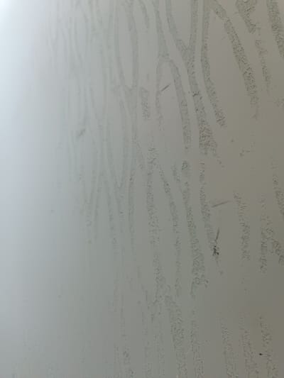 The image displays a close-up of a textured, light-colored surface with faint, irregular, vertical patterns. The texture appears somewhat rough and possibly dusty or weathered. The lighting suggests a diffused light source, casting minimal shadows. There are a few small, dark specks on the surface, possibly debris. The image does not contain any discernible objects, people, or actions that would allow for identification of a specific location in Dimitrovgrad, Russia, or any other city. The abstract nature of the texture prevents any meaningful contextual interpretation.