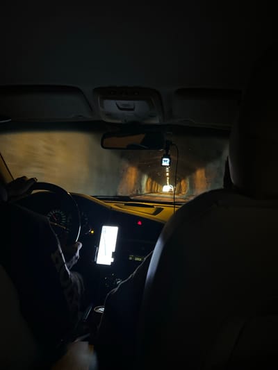 The media file shows a view from inside a vehicle, looking towards the dashboard and out a window. The perspective is from the driver's seat, with a hand on the steering wheel visible in the foreground. The scene is dark, suggesting it is nighttime. The vehicle appears to be traveling through a tunnel, indicated by the bright lights visible in the distance and the reflective, somewhat misty walls of the tunnel.

On the dashboard, there is a small screen, possibly a GPS or dashboard camera display, and other buttons and controls typical of a car's interior. A dashcam is mounted near the rearview mirror. The overall ambiance is one of travel through an enclosed, illuminated space. The lighting within the tunnel is yellowish, creating a slightly surreal or atmospheric effect. The image's orientation is rotated, as if the vehicle is traveling on its side.

There is visible text on a dark surface behind the driver, appearing to be part of a car's console. It reads "ERROR" and "CD". There is also text on the driver's sleeve, which is partially obscured but appears to say "HONDA" in large, white letters.

The location context is Horda, Norway. Given the dark interior and the tunnel setting, it's likely a nighttime drive in a region that experiences long nights, such as Norway during certain times of the year. The weather is not directly discernible, but the misty appearance in the tunnel could suggest damp conditions. No specific emotions are conveyed, but the image captures a moment of solitary travel.