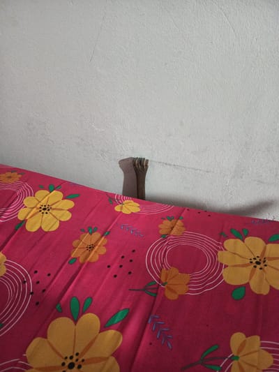 The image shows a partially visible bed frame with a floral patterned bedsheet against a white wall. The location is unknown, and there is no verifiable information to suggest it is in Quevedo, Ecuador.